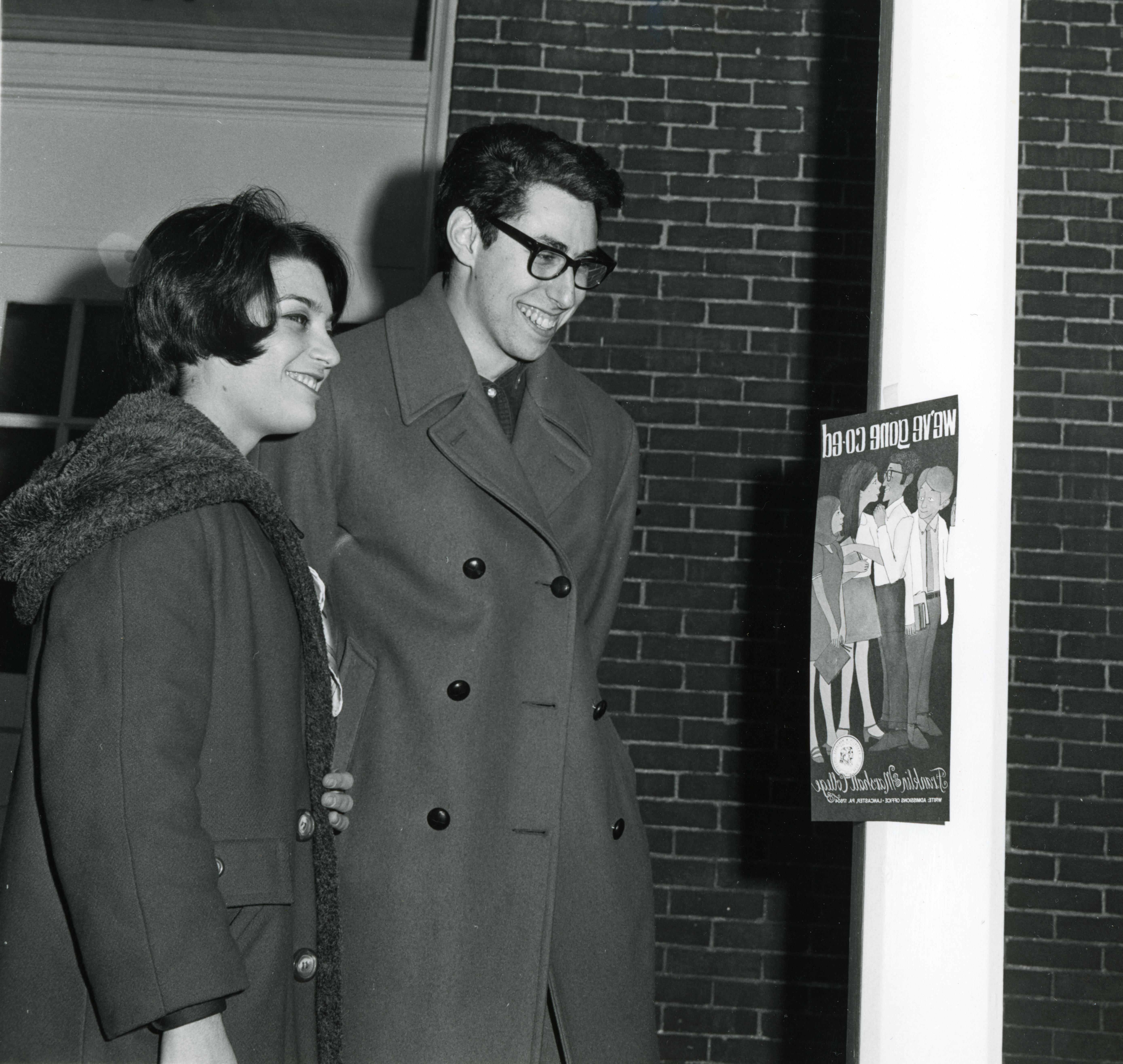 Two students looking at a poster reading "We've gone coed." Notes on the verso suggest that the photograph was printed in an F&M出版.